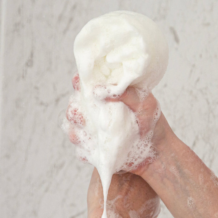 Hands holding a lathered bar of soap against a light background
