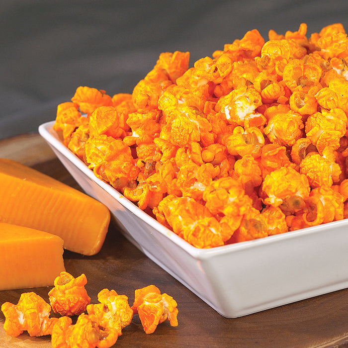 cheddar cheese popcorn displayed in a white serving dish next to slices of cheddar cheese