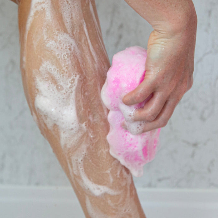 Person scrubbing leg with a pink sponge in a bathtub