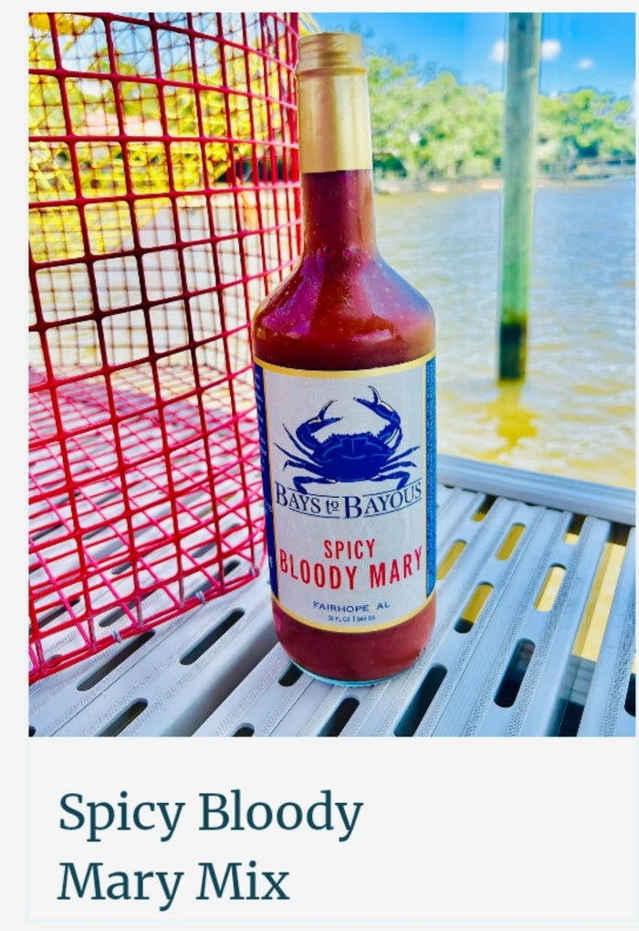 A bottle of Bay's of Bayou's Spicy Bloody Mary Mix sauce standing on a metal table outdoors near water, with a red wire fence on the left and a white text banner at the bottom reading 'Spicy Bloody Mary Mix'.
